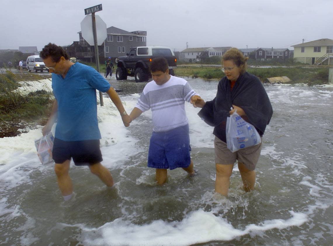 Sally and Phillip Adams of Richmond, Virginia, walk down a flooded section of Highway 12 in Kitty Hawk, NC, with son Brian, 18, as heavy surf churned over dunes eroded by the constant pounding of Hurricane Dennis in 1999.
