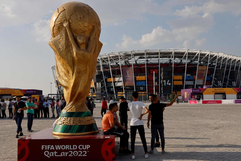 People pose for photos next to a giant replica on the World Cup trophy in front of Stadium 974 on November 18, 2022, in Doha, Qatar. (Photo by DAVID GANNON/AFP via Getty Images)