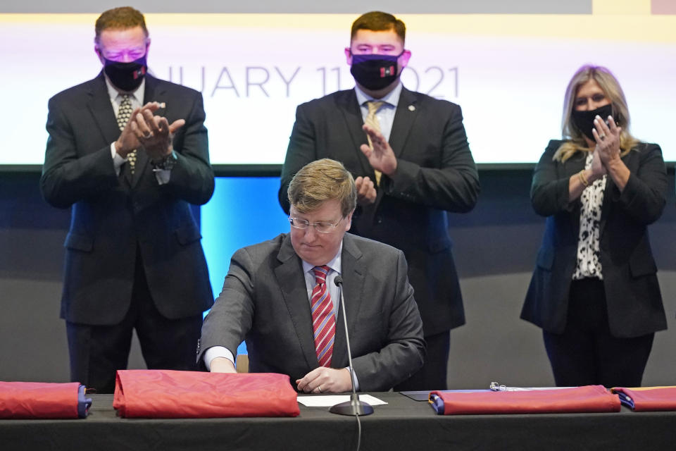 Flag commission members applaud as Gov. Tate Reeves finishes signing into law, legislation that creates the new state flag during a ceremony in Jackson, Miss., Monday, Jan. 11, 2021. The new banner features a magnolia at the center and replaces the retired flag that was the last state flag in the U.S. that included the Confederate battle emblem. (AP Photo/Rogelio V. Solis)