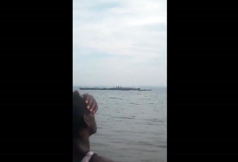 This framegrab taken from mobile phone footage shows a person on the shore watching the search and rescue of people standing on the capsized hull of a ferry, on Lake Victoria, Tanzania. The death toll rose above 100 on Friday Sept. 21, 2018, after the ferry capsized and sank on Lake Victoria, Tanzania state radio reported. (Mteule Gosberth Kahangile via AP)