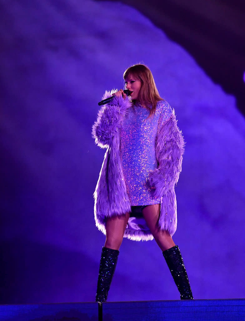 Taylor Swift performing on stage wearing a sequined outfit and feathered coat