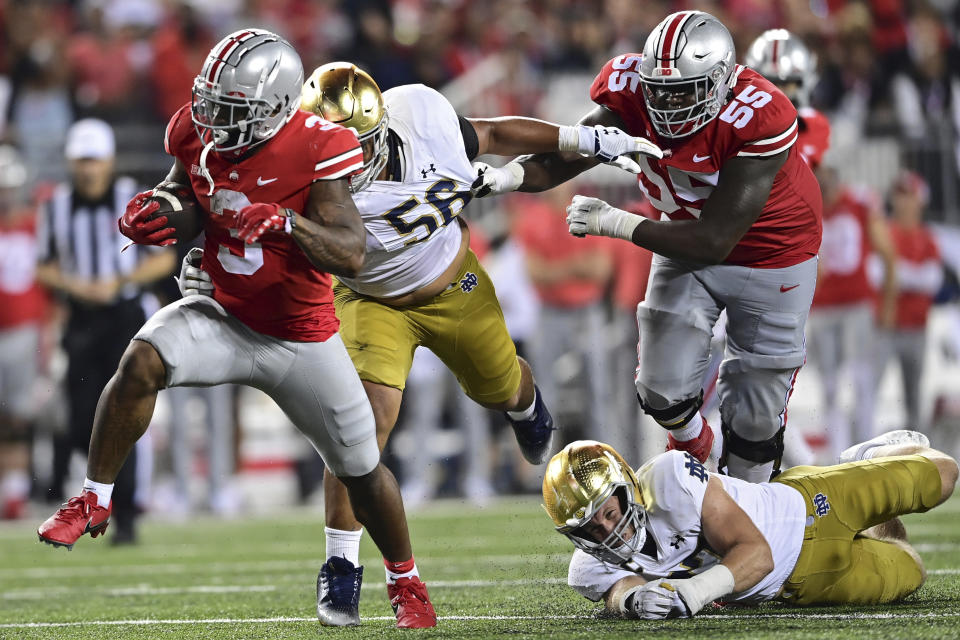 Ohio State running back Miyan Williams, left, runs the ball away from Notre Dame defensive lineman Howard Cross III, second from left, and linebacker JD Bertrand, bottom, during the fourth quarter of an NCAA college football game Saturday, Sept. 3, 2022, in Columbus, Ohio. (AP Photo/David Dermer)