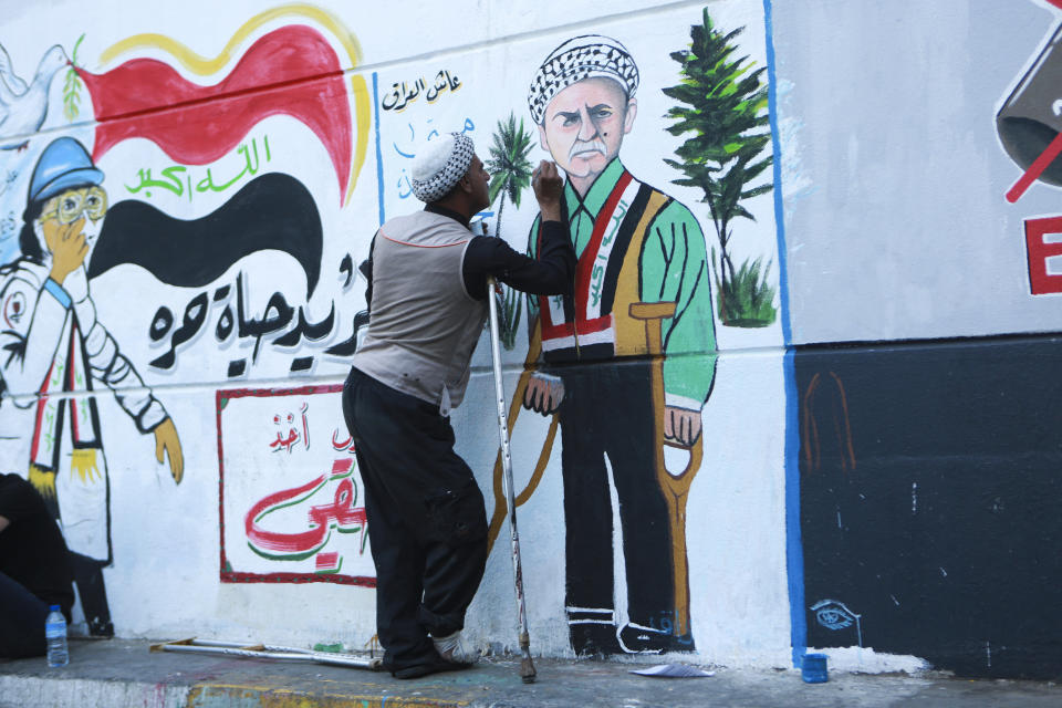 In this Sunday, Nov. 17, 2019 photo, a protestor adds some details and facial expressions to graffiti that was drawn by an Iraqi artist, at the Saadoun Tunnel, in Baghdad, Iraq. The tunnel that passes under Baghdad’s landmark Tahrir Square has become an ad hoc museum for Iraq's revolution: Young artists draw images and murals that illustrate the country’s tortured past, and the Iraq they aspire to. (AP Photo/Hadi Mizban)