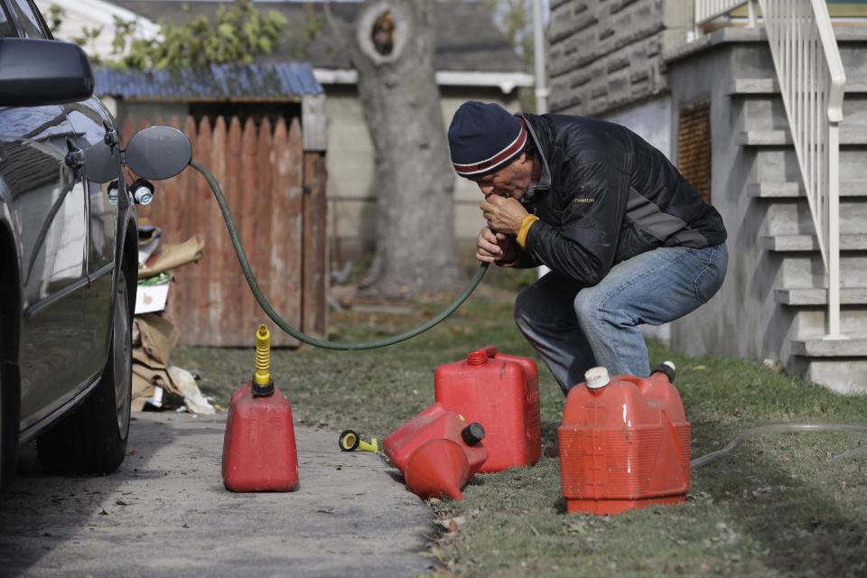 Chris Zaturoski uses a garden hose to attempt to siphon gasoline from his car to use in a generator at his house which is without power in the wake of superstorm Sandy on Thursday, Nov. 1, 2012, in Little Ferry, N.J. The hose was too big to fit into the gas tank of the car. New Jersey residents across the state were urged to conserve water. At least 1.7 million customers remained without electricity. (AP Photo/Mike Groll)