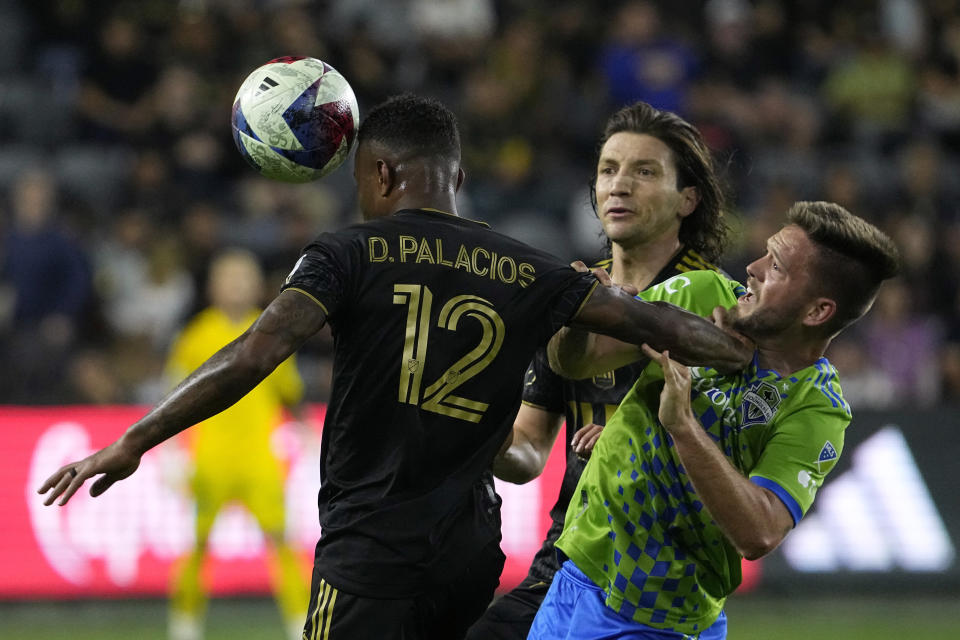 Los Angeles FC defender Diego Palacios, left, heads the ball as he pushes Seattle Sounders midfielder Kelyn Rowe, right, away while midfielder Ilie Sanchez watches during the first half of a Major League Soccer match Wednesday, June 21, 2023, in Los Angeles. (AP Photo/Mark J. Terrill)