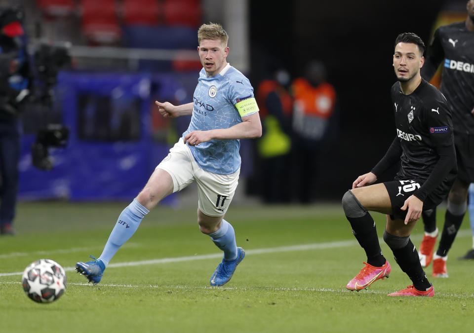 Kevin De Bruyne del Manchester City pasa el balón frente a Ramy Bensebaini del Borussia Moenchengladbach en el partido por los octavos de final de la Liga de Campeones, el martes 16 de marzo de 2021, en Budapest. (AP Foto/Laszlo Balogh)