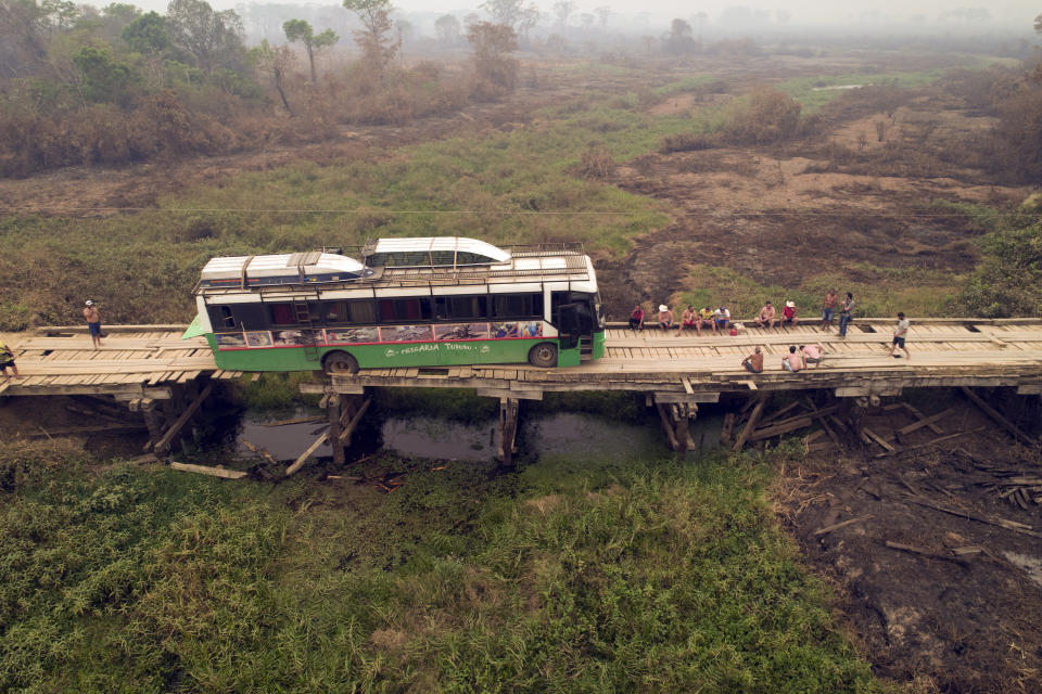 Tourists sit on a bridge railing after their sports fishing tour bus became stuck on a bridge damaged by wildfires, on the Trans-Pantanal highway in the Pantanal wetlands near Pocone, Mato Grosso state, Brazil, Friday, Sept. 11, 2020. Both sides of the highway usually feature pools of water, even in its dry season. (AP Photo/Andre Penner)