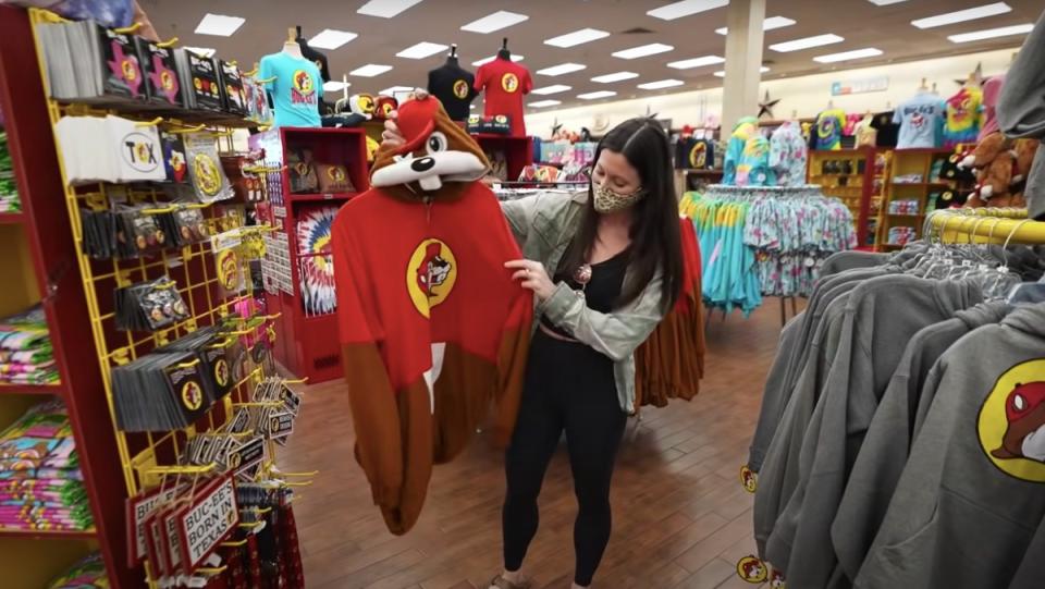 YouTuber Kara from the travel vlog channel Kara and Nate holds up a Bucky the beaver costume at a Buc-ee's in Texas, the largest gas station in the world.
