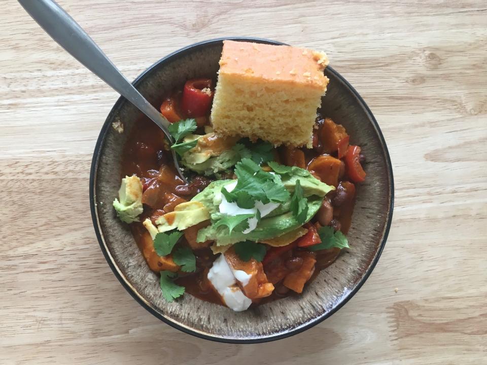 CHILI with sweet potato, red pepper, and cornbread in brown bowl and spoon