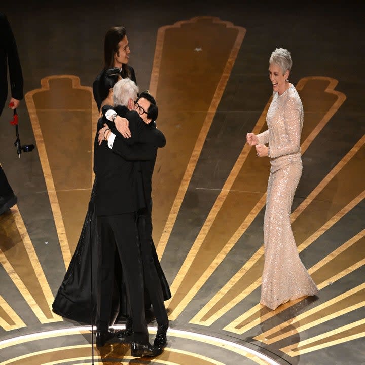 Jamie Lee Curtis smiling as two men embrace onstage