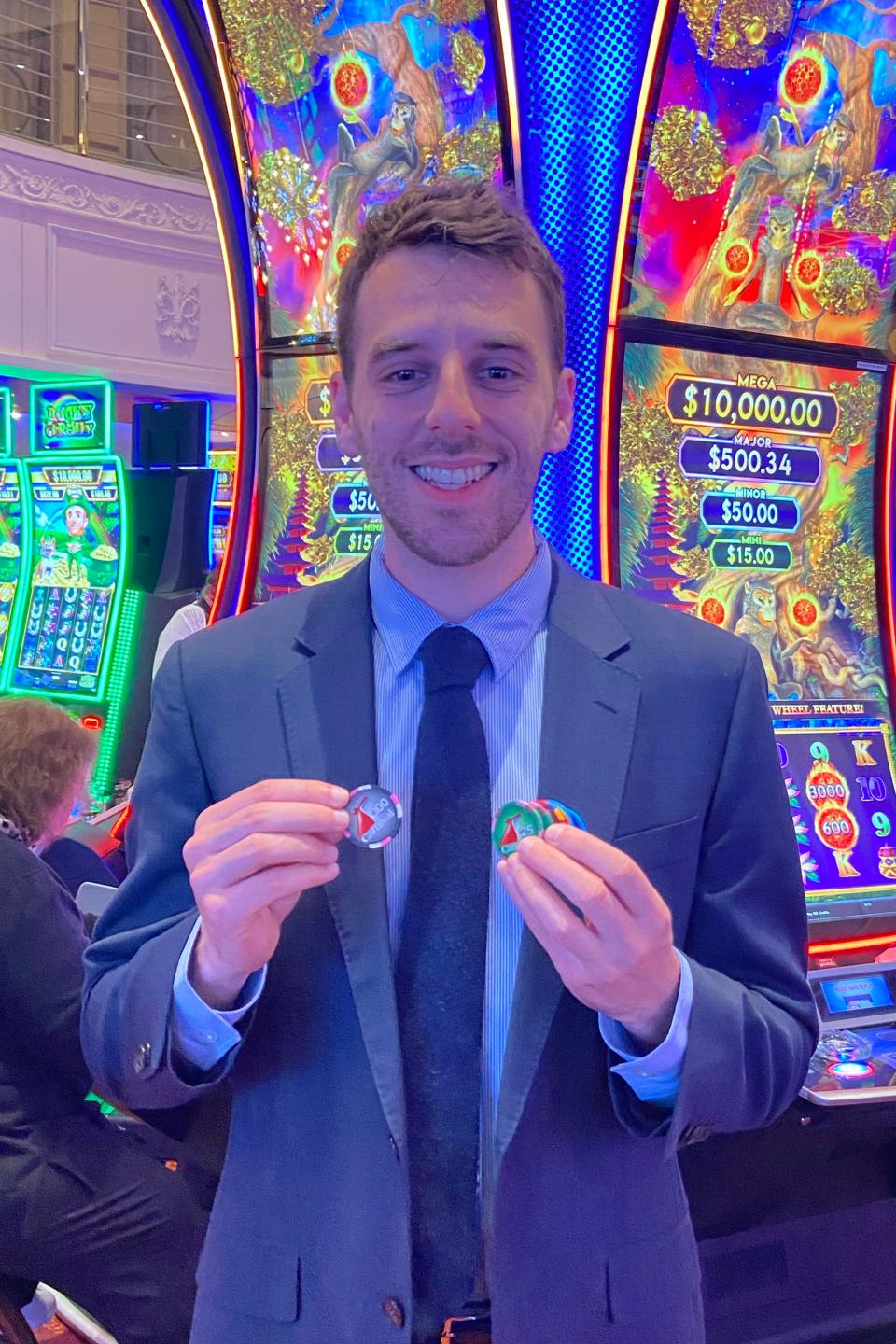 Man in a suit holding casino chips, standing in front of slot machines