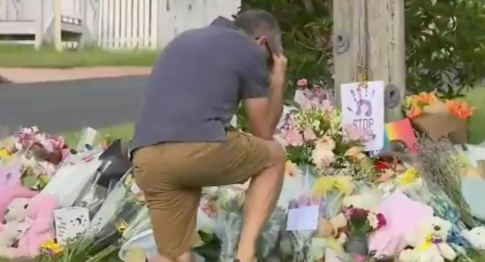 A man kneels near a memorial for the Clarke family in Camp Hill.