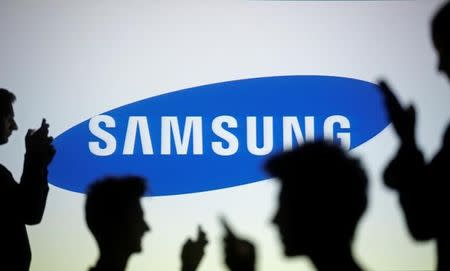 People are silhouetted as they pose with mobile devices in front of a screen projected with a Samsung logo, in this illustration picture taken on October 29, 2014. REUTERS/Dado Ruvic/Illustration/Files