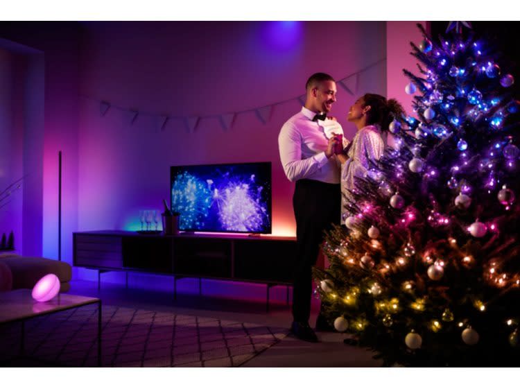 Man and woman dancing near Christmas tree with Philips Hue Festavia String Lights on it.