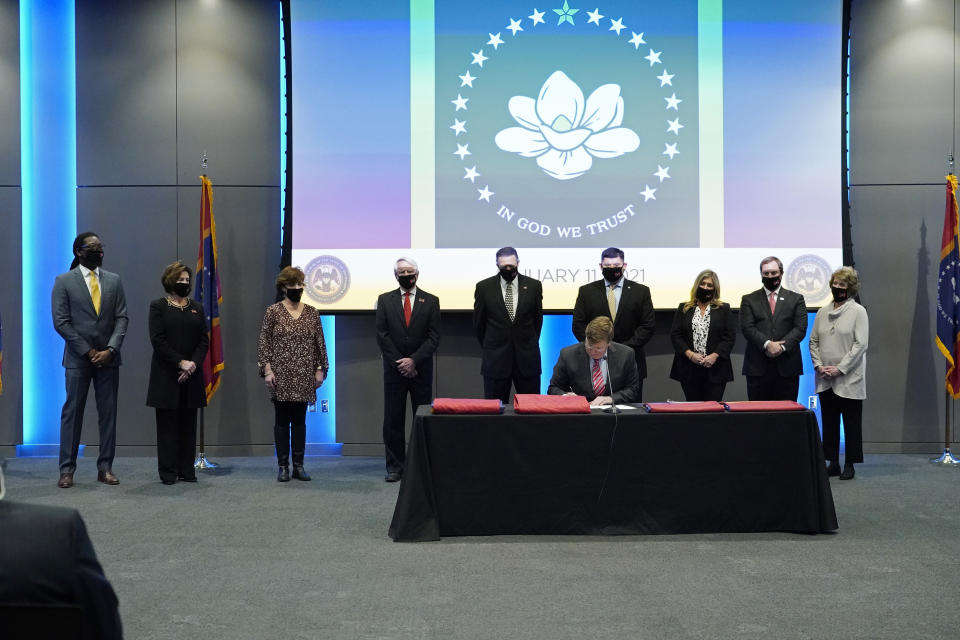 Flag commission members stand behind Gov. Tate Reeves as he signs into law, legislation that creates the new state flag during a ceremony in Jackson, Miss., Monday, Jan. 11, 2021. The new banner features a magnolia at the center and replaces the retired flag that was the last state flag in the U.S. that included the Confederate battle emblem. (AP Photo/Rogelio V. Solis)