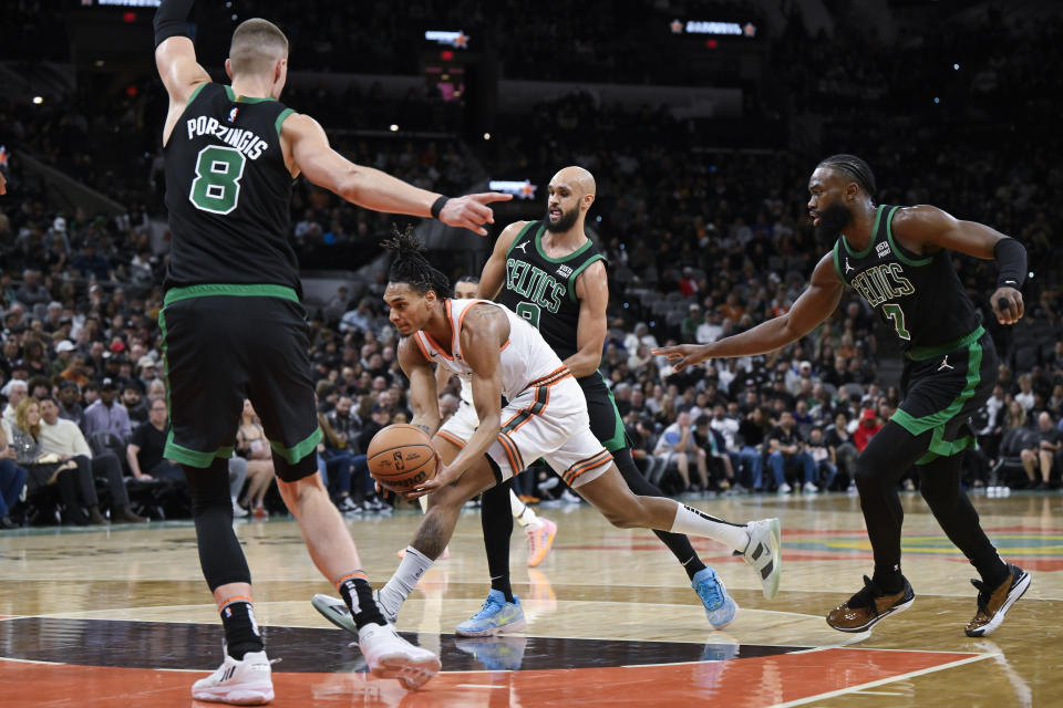 San Antonio Spurs' Devin Vassell drives to the basket as he is defended by Boston Celtics' Kristaps Porzingis (8), Jaylen Brown (7) and Derrick White during the first half of an NBA basketball game, Sunday, Dec. 31, 2023, in San Antonio. (AP Photo/Darren Abate)