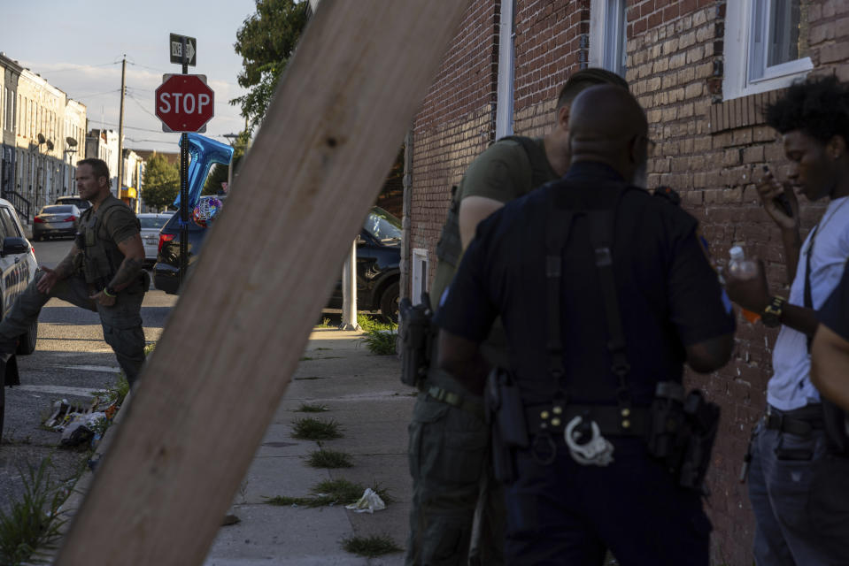 Police officers question a boy during a vigil for Antonio Lee, Friday, Aug. 18, 2023, in Baltimore. Lee, 19, was shot and killed while squeegeeing in Baltimore. (AP Photo/Julia Nikhinson)