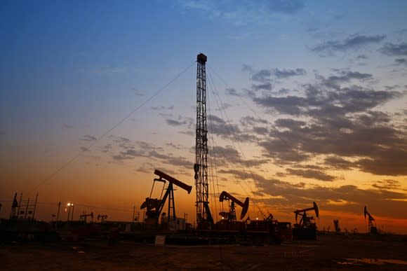 A drilling rig surrounded by oil pumps at sunset.