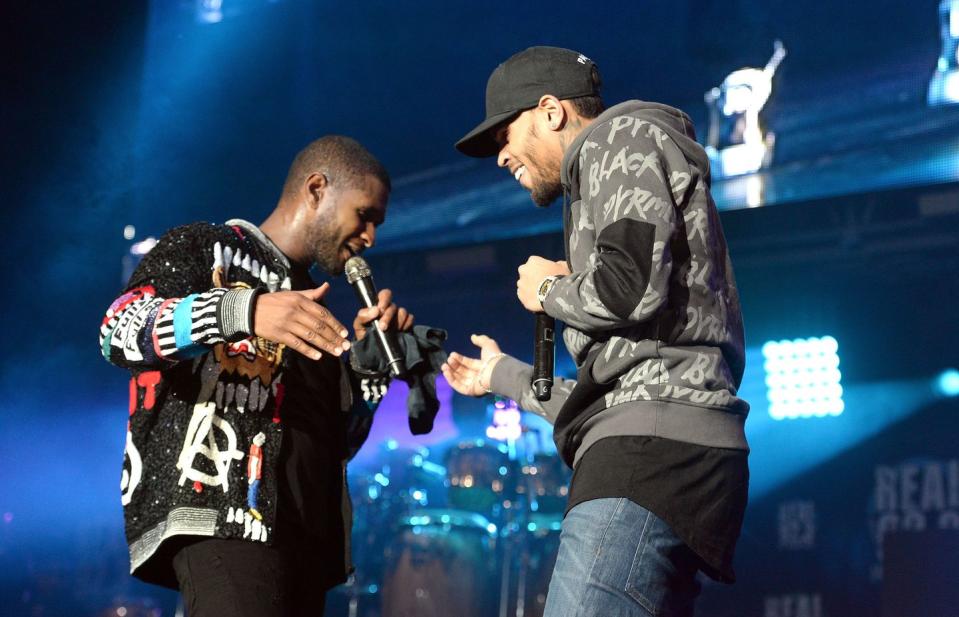 usher and chris brown shake hands while holding microphones and smiling on a stage