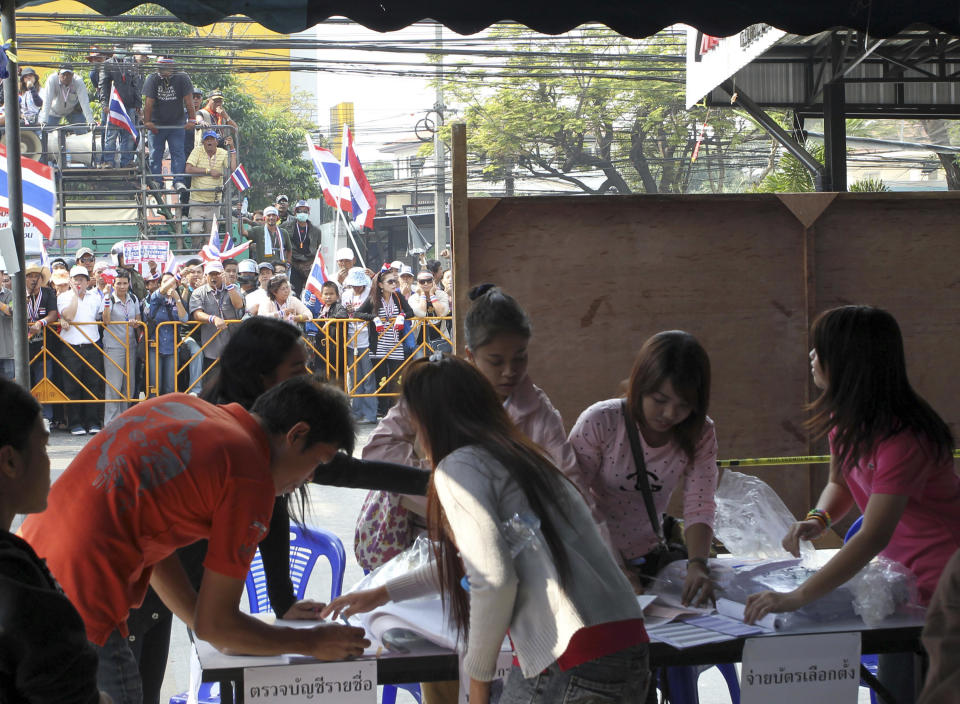 Anti-government protesters, left in background, stage a rally opposing an advance voting as officials work at a polling station in Bangkok Sunday, Jan. 26, 2014. The demonstrators trying to derail a contentious general election scheduled next week in Thailand swarmed dozens of polling stations Sunday, chaining doors and gates shut and blocking hundreds of thousands of voters from casting advance ballots in the latest blow to the country's increasingly embattled government. (AP Photo/Apichart Weerawong)