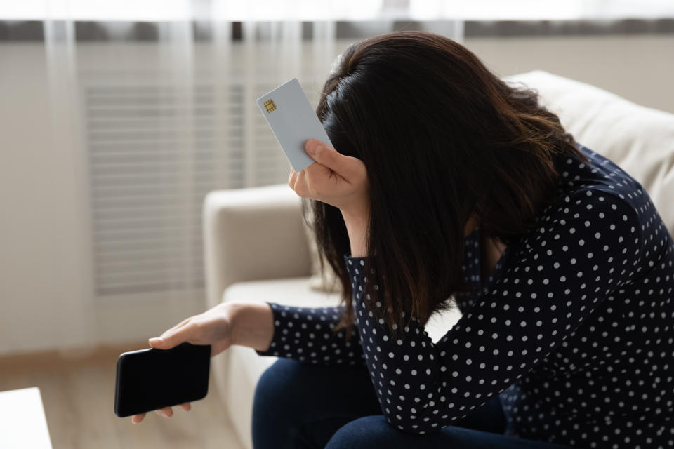 Close up unhappy frustrated Asian woman holding white empty mock up plastic card and phone, touching head, crying, having problem with credit card, loss money, internet fraud and scam concept