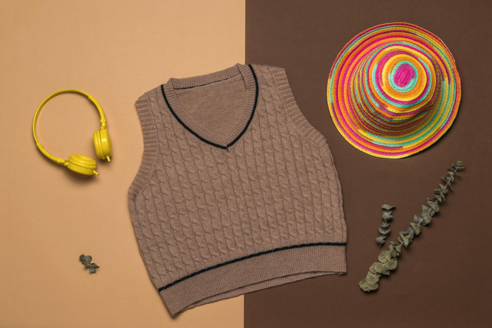 A hat, a knitted vest and headphones on a two-tone background. Fashionable classic knitted clothing.