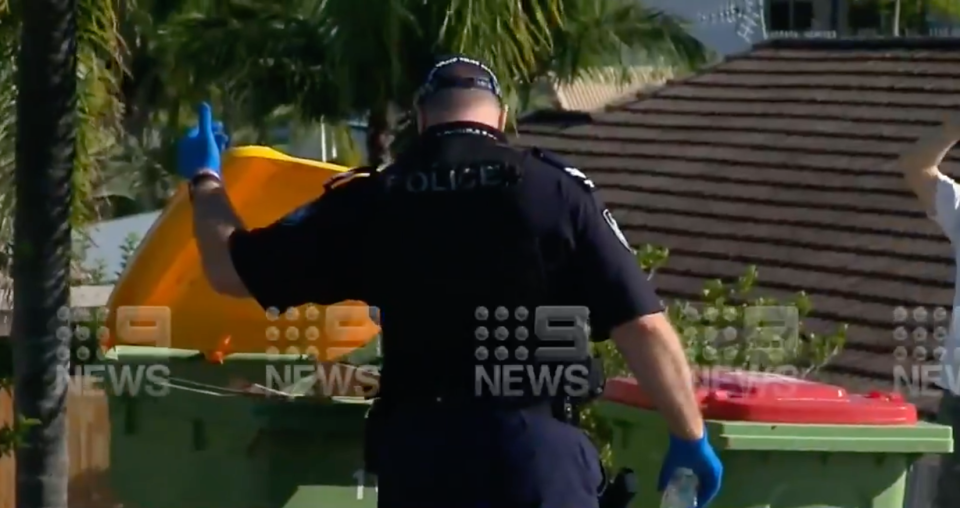 A police officer checks nearby bins for potential evidence. Source: Nine News