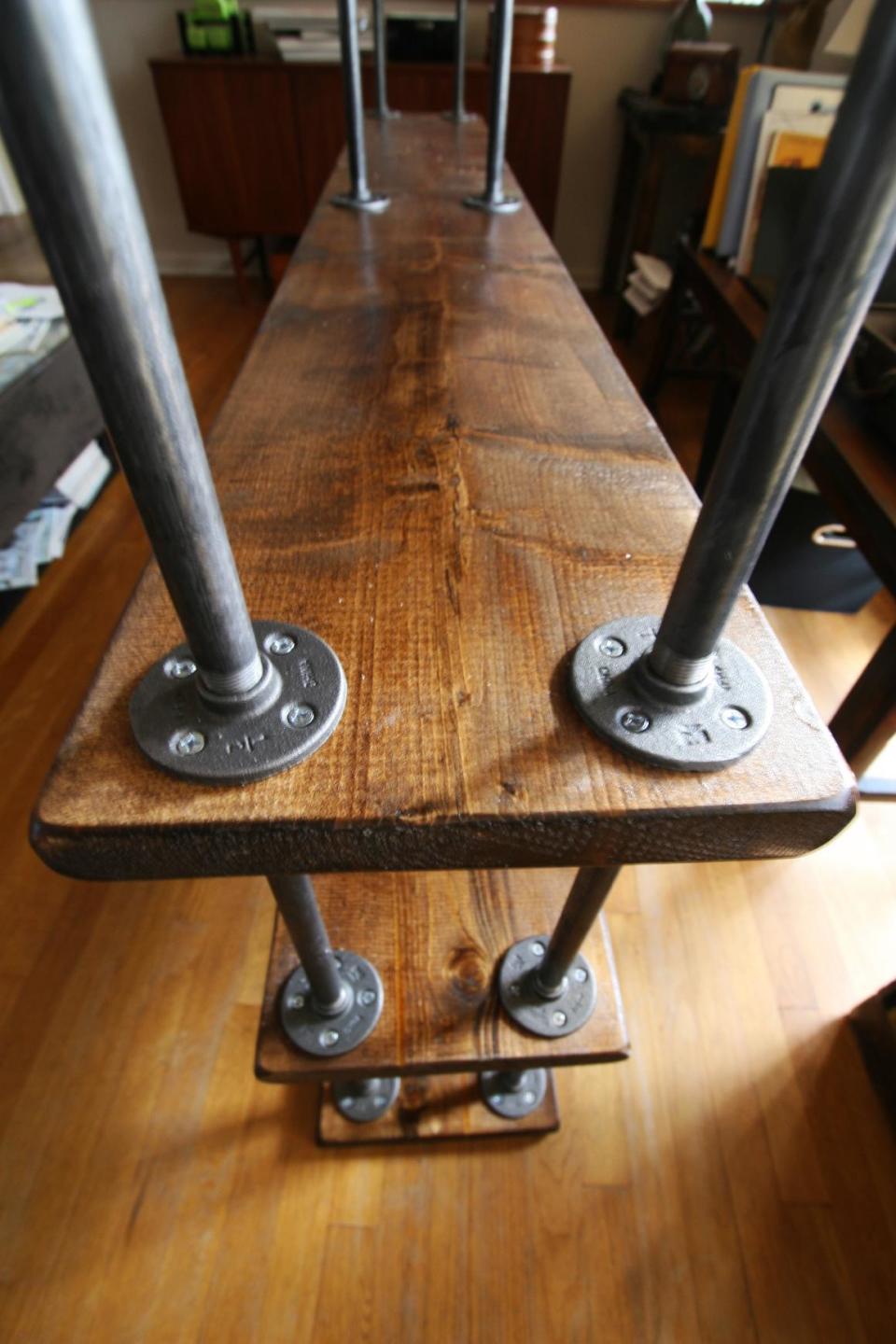 This undated photo shows the creation of a DIY bookshelf with multiple pipes attached to the flanges on the three levels of a book shelf. Industrial-style shelving units and tables made from planks of wood and plumbing parts are gorgeous and trendy, and can cost thousands of dollars. But creating custom-designed, industrial furniture yourself is surprisingly easy. (AP Photo/Ted Anthony)