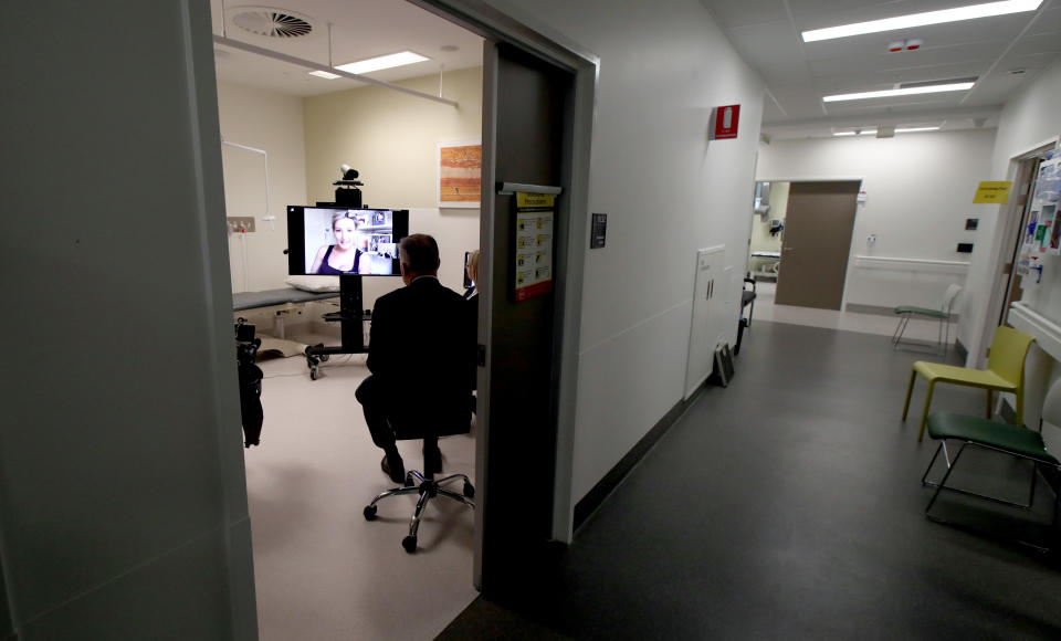 A doctor utilising a new video conferencing clinic at the Royal Adelaide Hospital to speak with a cystic fibrosis patient who is up on a TV screen.