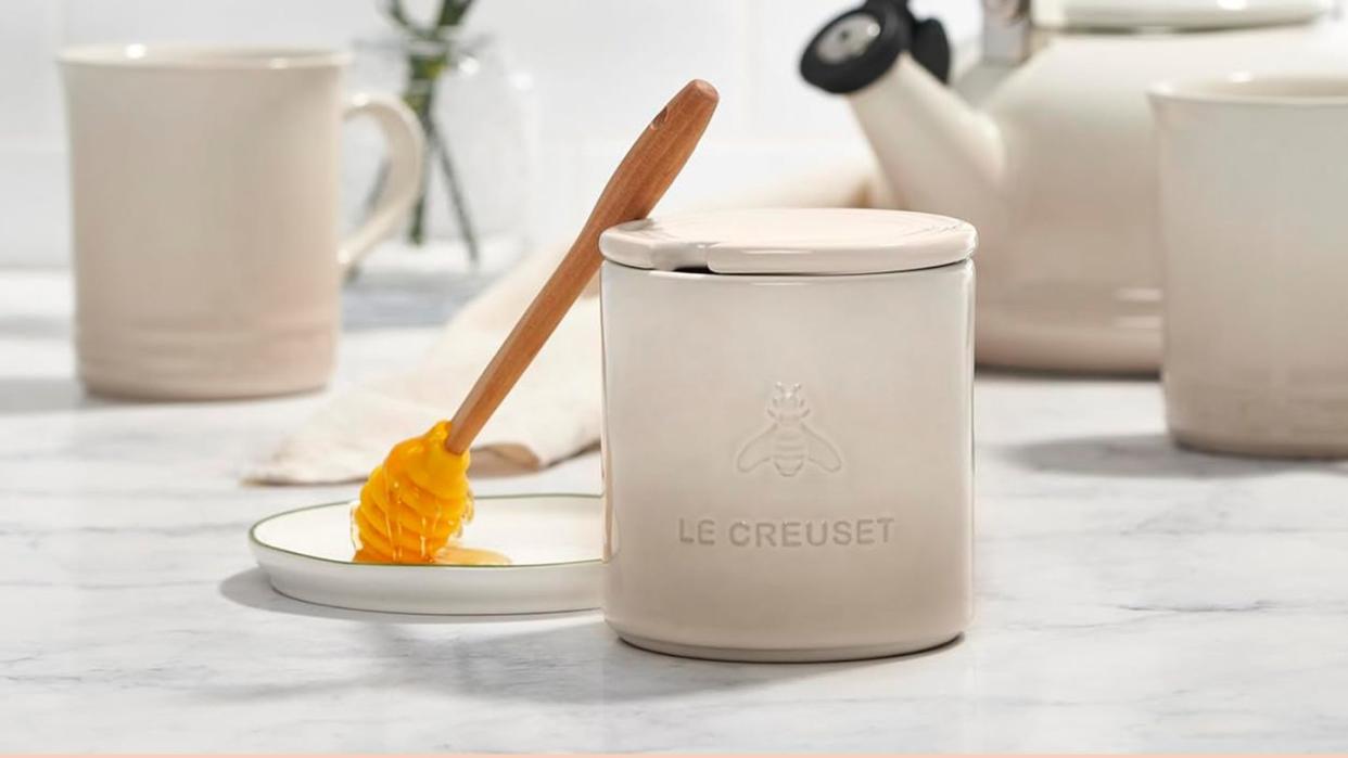 a white le creuset honey pot with a spoon