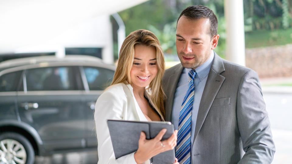 Business couple at the car dealership buying a car and looking at models on a tablet computer.