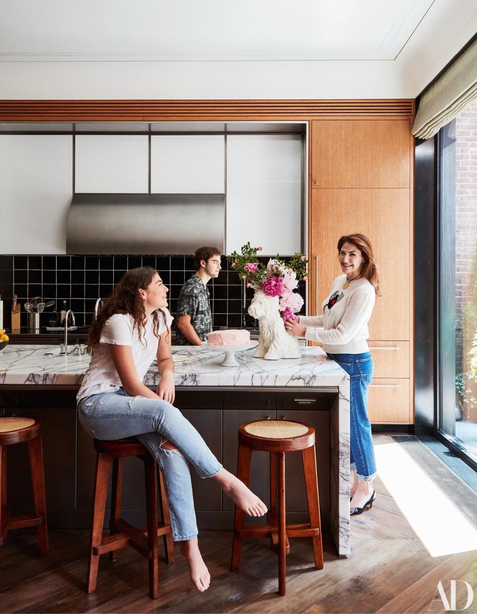 Allison, wearing a Dior sweater and jeans, and two of her children gather around the kitchen island; fashion styling by Marina Muñoz.