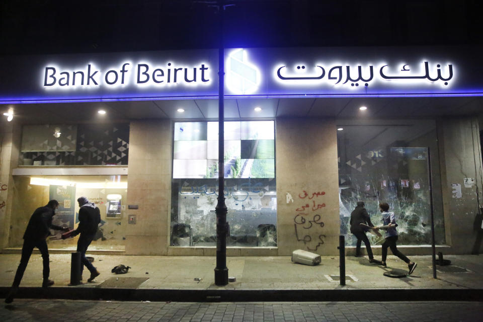 Anti-government protesters smash a bank widows, during ongoing protests against the Lebanese central bank's governor and against the deepening financial crisis, at Hamra trade street, in Beirut, Lebanon, Tuesday, Jan. 14, 2020. Lebanese security forces lobbed tear gas at protesters who responded with rocks outside the country's central bank Tuesday, a violent turn after demonstrators returned to the streets following a weekslong lull. (AP Photo/Hussein Malla)