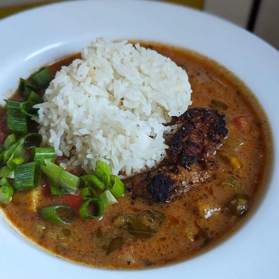 a plate of of gumbo with rice on top and scallions