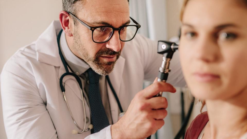 ENT doctor checking ear with otoscope of woman patient at hospital.