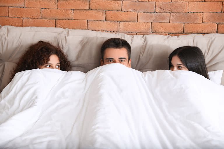 Man with two beautiful women in bed. Polyamory concept