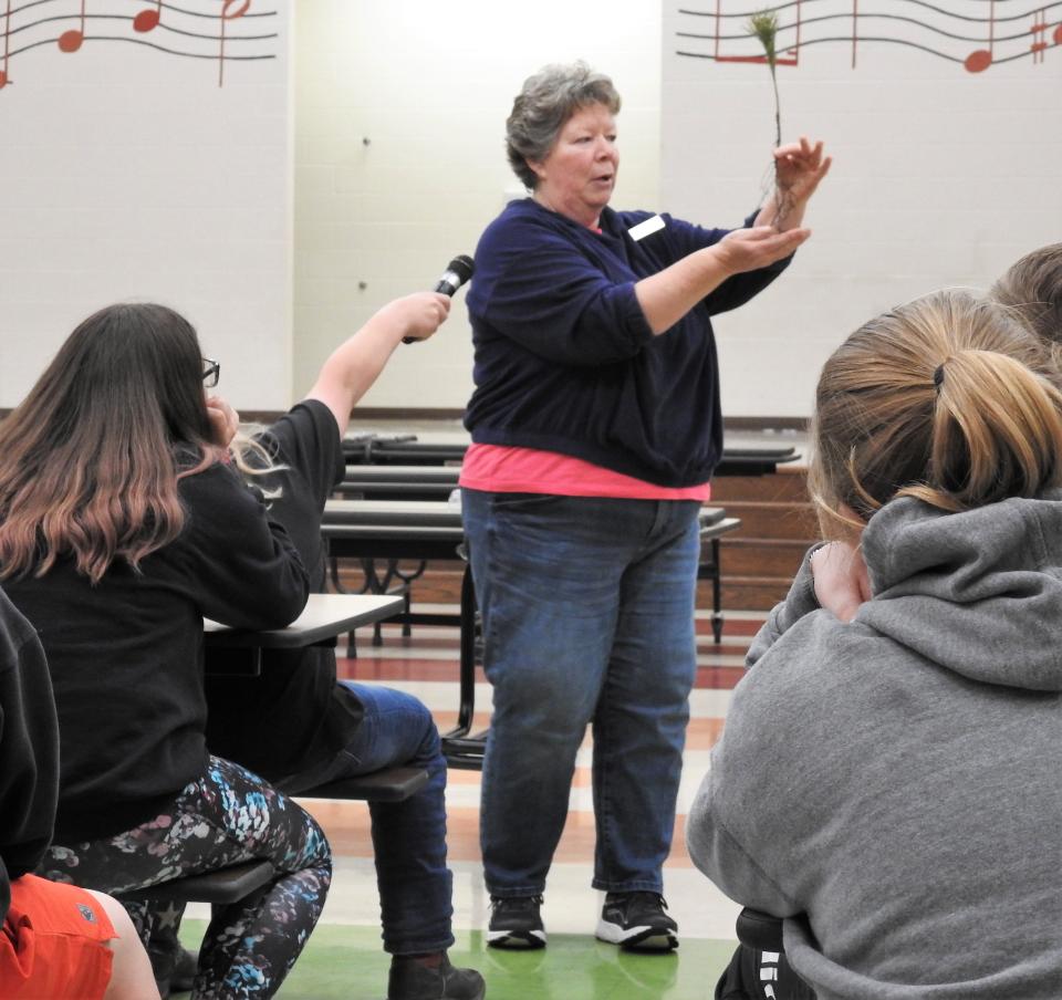 Deb Bigelow shows sixth grade students at Coshocton Elementary School a tree seedling during a recent Arbor Day presentation. All received a sapling to take home and plant.