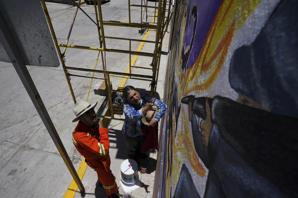 El artista mexicano Jesús Rodríguez, a la derecha, instruye a Luis Manuel Vélez durante una sesión de pintura frente a un mural que Rodríguez está pintando en la fachada de un auditorio en San Salvador, México, el sábado 30 de julio de 2022. (Foto AP/Fernando Llano)