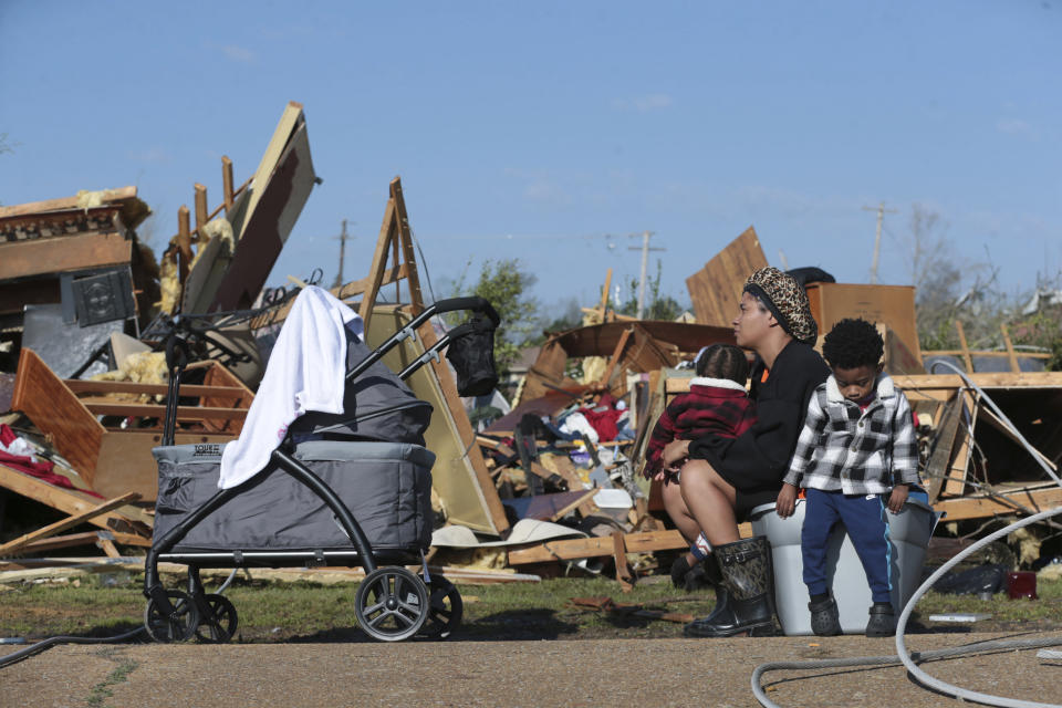 Melanie Childs of Amory, Miss., sits on a bucket and holds her two children, Mila, 1, left, and Major, 2, as they view whats left of her grandfather, Barrie Young, home Saturday 25, 2023. Emergency officials in Mississippi say several people have been killed by tornadoes that tore through the state on Friday night, destroying buildings and knocking out power as severe weather produced hail the size of golf balls moved through several southern states. (Thomas Wells/The Northeast Mississippi Daily Journal via AP)