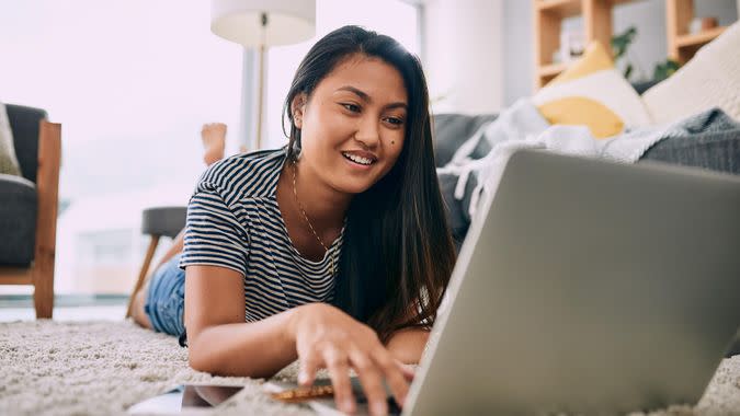 Shot of a young woman using a laptop while relaxing in the living room at home.