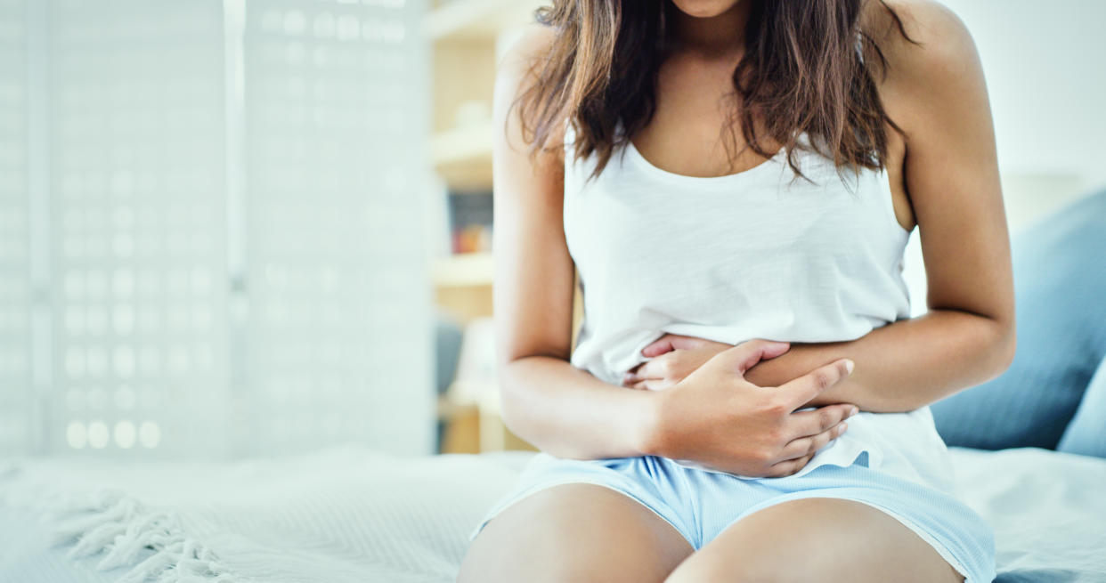 Shot of an unrecognizable woman suffering from stomach cramps in her bedroom