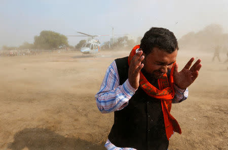 A supporter covers himself from the rising dust caused by the helicopter of Keshav Prasad Maurya, the Uttar Pradesh state's president for the ruling Bharatiya Janata Party (BJP), during an election campaign rally in Bah, in the central state of Uttar Pradesh, India, February 2, 2017. REUTERS/Adnan Abidi