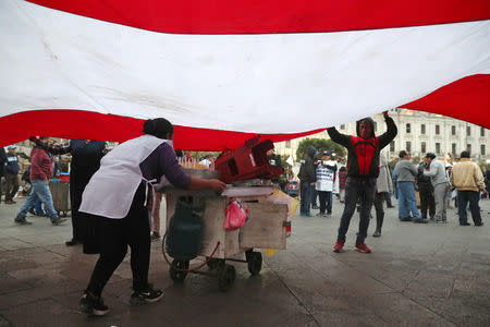 A street vendor passes under a Peruvian flag during a protest to support Peru's President Martin Vizcarra after he asked the Congress for a new vote of confidence in his Cabinet in Lima, Peru September 18, 2018. REUTERS/Guadalupe Pardo