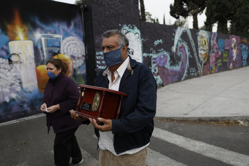 Gustavo Briseno Garcia, accompanied by his wife Leticia Pinera Santana, carries the urn containing the ashes of his father, Manuel Briseno Espino, 78, who died from complications due to COVID-19, in the Iztapalapa district of Mexico City, Wednesday, April 22, 2020. Due to social distancing restrictions, the seven family members from three generations who lived with him marked his passing with quiet prayers at home, unable to invite his many friends or other relatives, or to bury him in the cemetery plot with his late wife of 49 years, Consuelo Garcia Rodriguez. (AP Photo/Rebecca Blackwell)