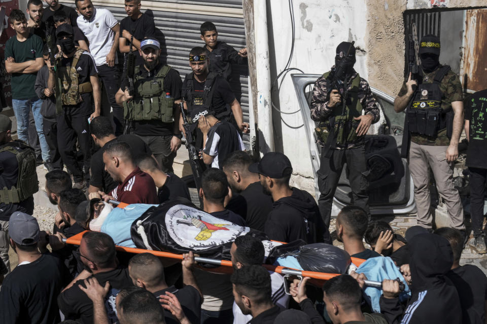 Palestinian gunmen fire into the air as mourners carry the body of an Islamic Jihad militant during his funeral in the Nur Shams refugee camp near the West Bank town of Tulkarem, Sunday, April 21, 2024. The Palestinian Red Crescent rescue service said 14 bodies have been recovered from the Nur Shams urban refugee camp since an Israeli military operation began in the area Thursday night. The Islamic Jihad militant group confirmed the deaths of three members. Another killed was a 15-year-old boy. The Israeli army said its forces killed 10 militants in the camp and surrounding areas while eight suspects were arrested. (AP Photo/Majdi Mohammed)