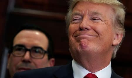 With Treasury Secretary Steve Mnuchin standing behind him, U.S. President Donald Trump smiles while listening to remarks before signing an executive order making it easier for Americans to buy bare-bones health insurance plans and circumvent Obamacare rules at the White House in Washington, U.S., October 12, 2017. REUTERS/Kevin Lamarque/Files