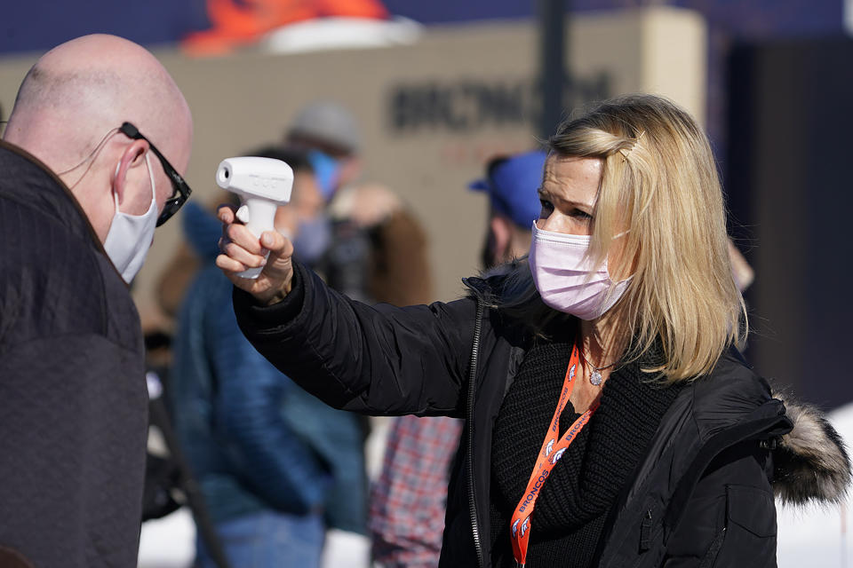 Rachel Deets, right, special events assistant for the Denver Broncos, uses a thermometer to take the temperature of beat writer Ryan O'Halloran before he can watch the team take part in drills during an NFL football practice at the team's headquarters Wednesday, Nov. 25, 2020, in Englewood, Colo. (AP Photo/David Zalubowski)