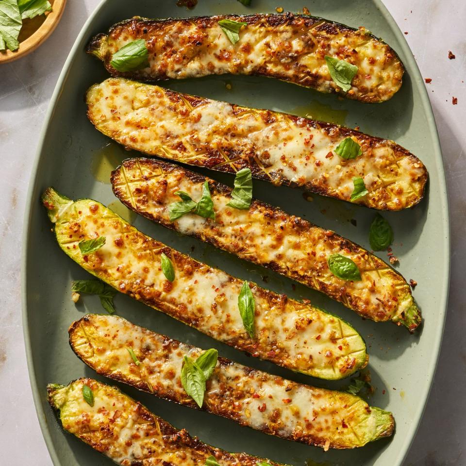 cheesy garlic zucchini steaks on a green platter topped with basil and red pepper flakes