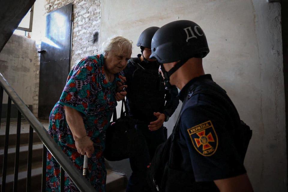 Emergency service members help an elderly woman at a site of an apartment building heavily damaged by a Russian missile strike (via REUTERS)