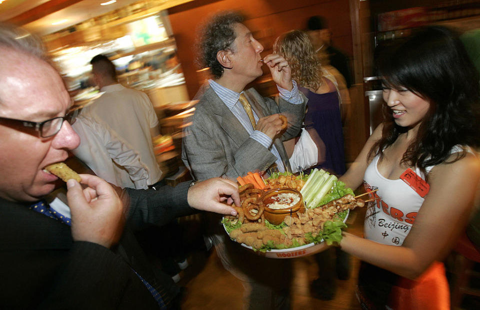 A Hooters waitress holding out a tray of food for customers.